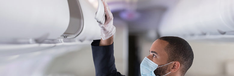 A masked cleaner wiping an overhead bin as part of a deep-cleaning and disinfecting performed before and after a flight.