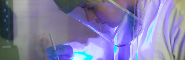 A scientist wearing personal protective equipment testing ultraviolet light on a surface in a laboratory.