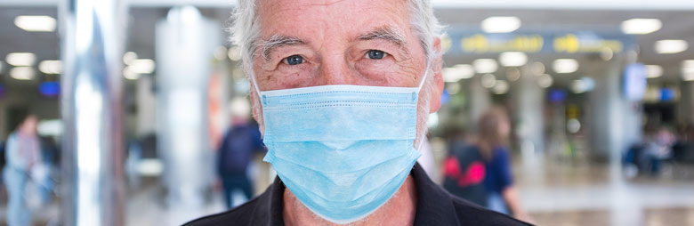 A passenger wearing a mask standing on a busy airport concourse on their way to their departure gate.