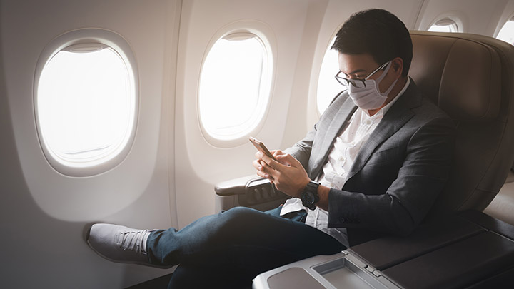 Photo of masked passenger reading study on his phone that shows risk of inflight infection is less than 1 in 2.7 million.