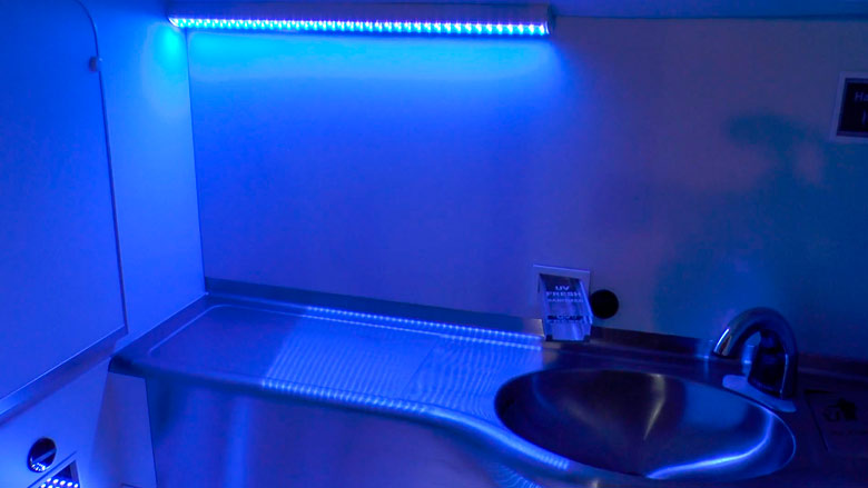 Ultraviolet lights automatically disinfecting the interior of an airplane lavatory after every use.