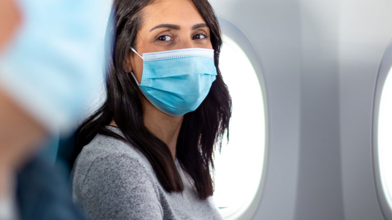 A masked passenger on an airplane. The airplane cabin design and airflow create the equivalent of more than 7 feet (2 meters) of physical distance between every passenger.